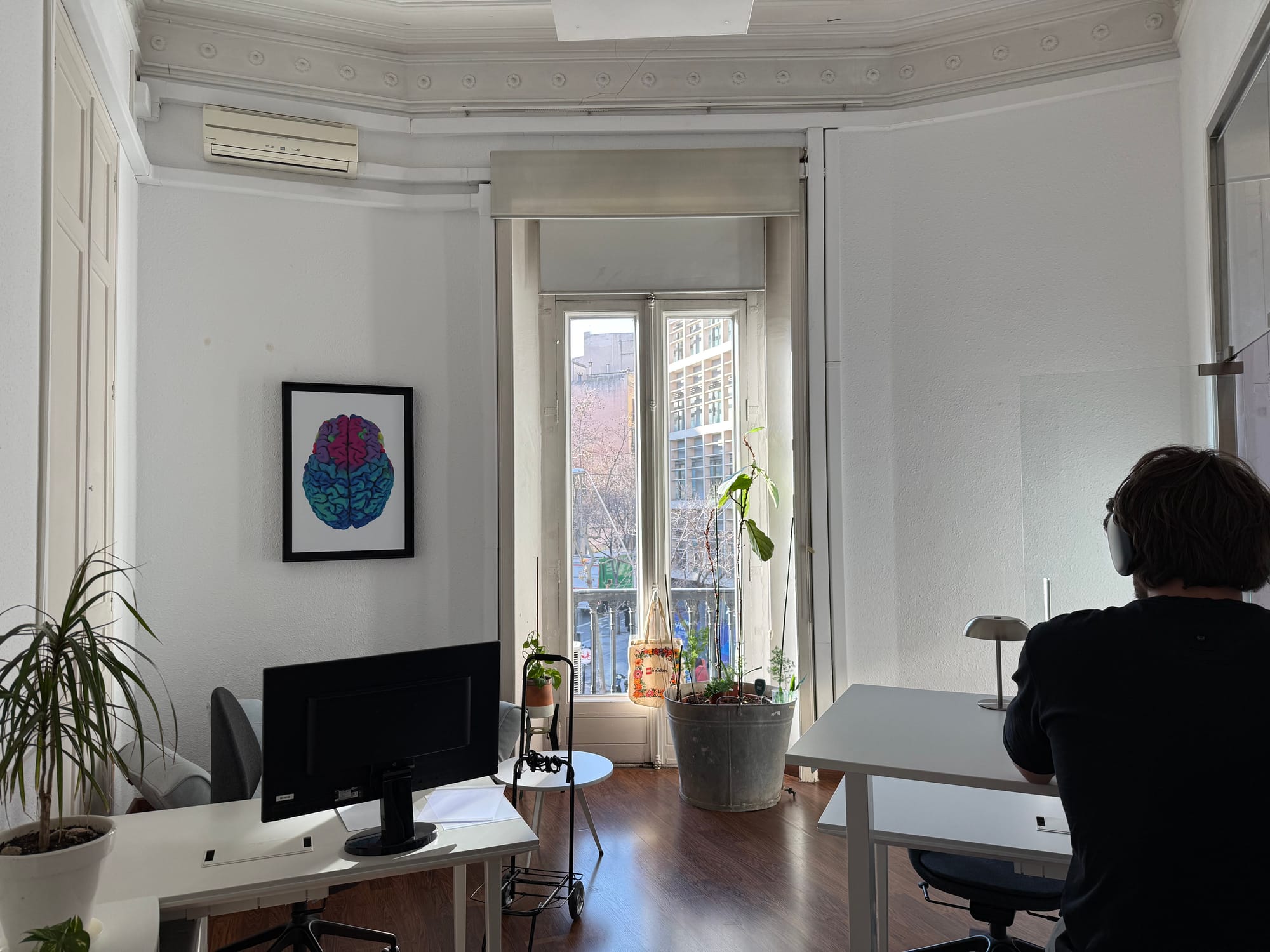 An Eixample 46 office with a member working at a desk, plants by the door, and a tall French window opening onto a narrow balcony