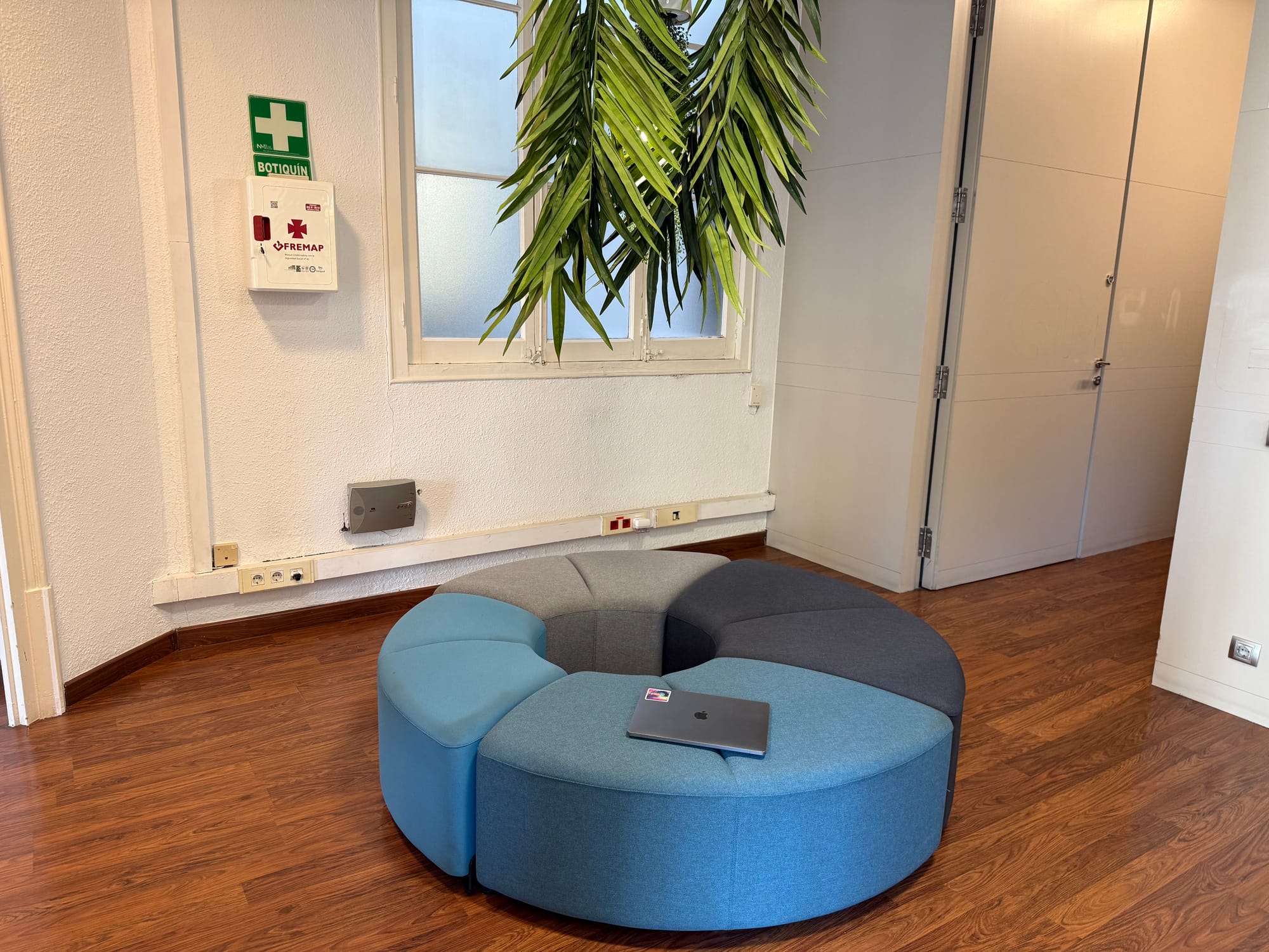 The round modular ottoman in soft blues and greys at Eixample 46, with a hanging palm above and the wooden floor beneath