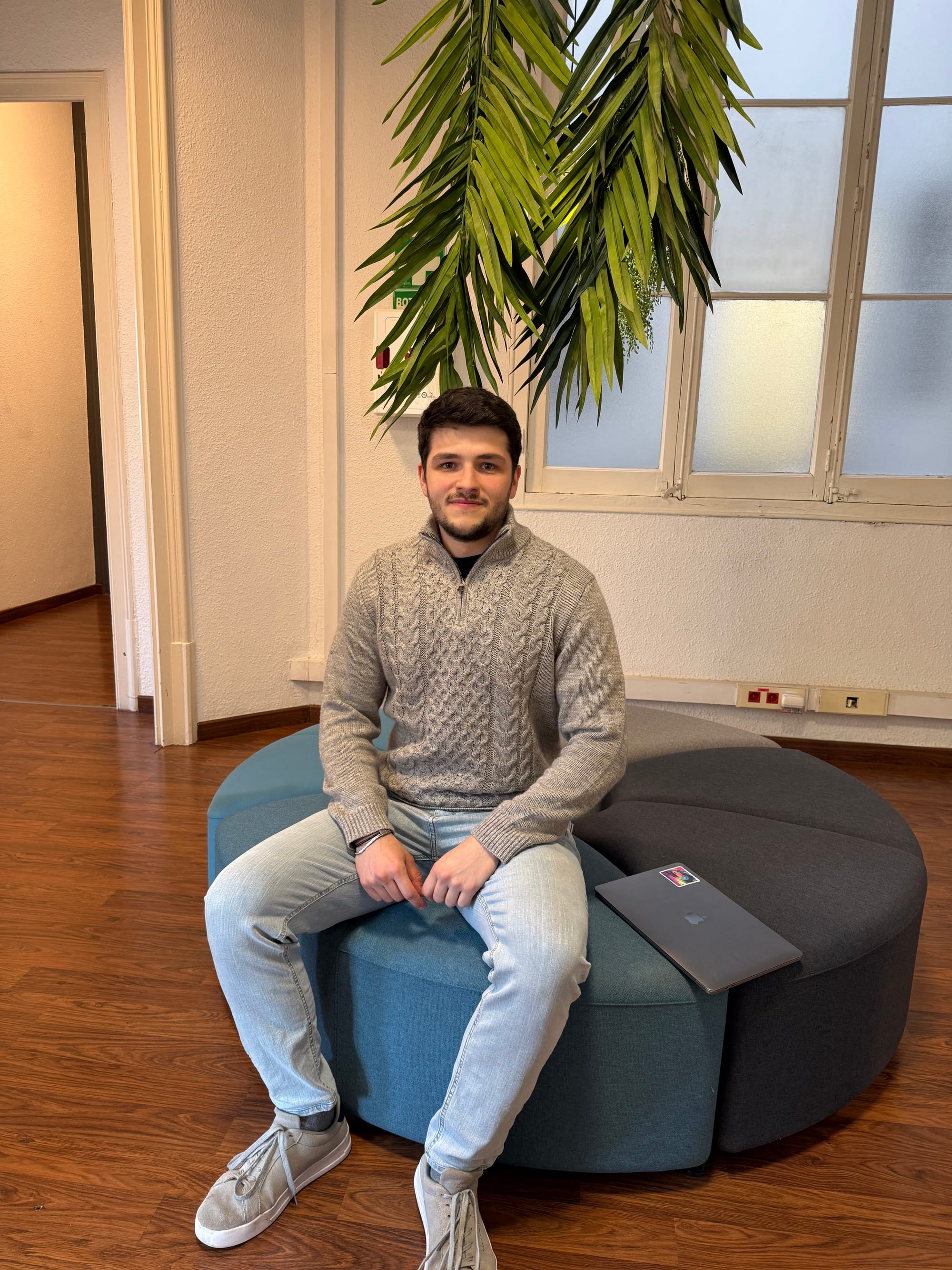 Bojan, the founder of Eixample 46, sitting on the round ottoman with a laptop beside him