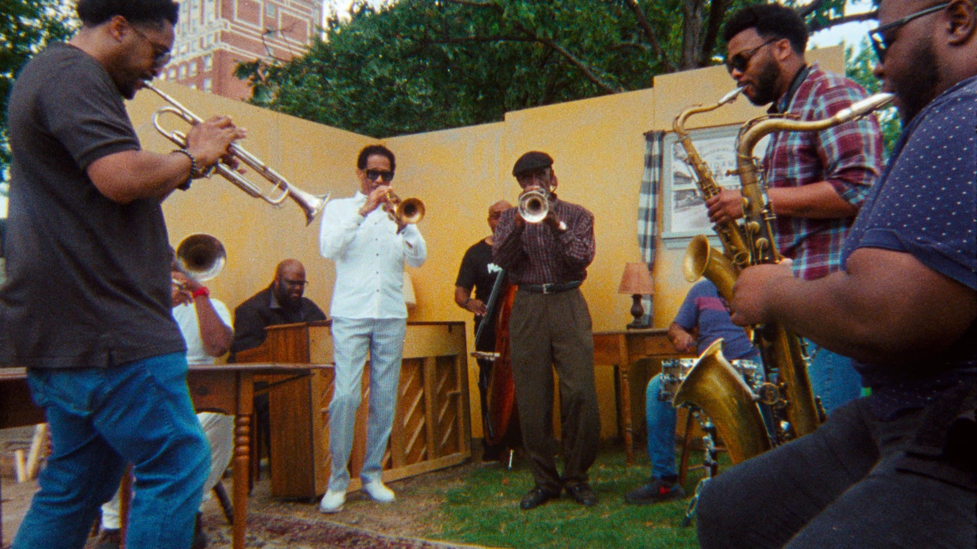 A jazz band performing outdoors on a stage with a decorated backdrop, featuring musicians playing the trumpet, saxophone, and piano.