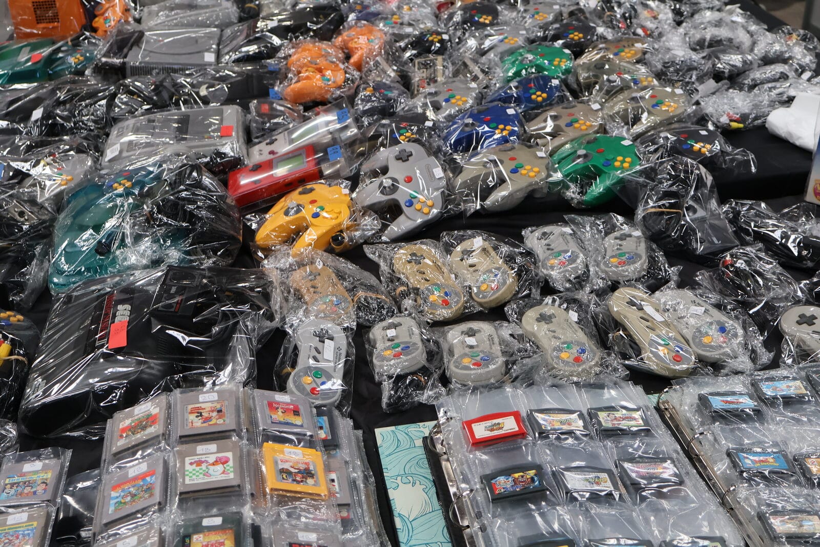 Stacks of vintage joypads and game cartridges, still in their bags, arranged on a market stall