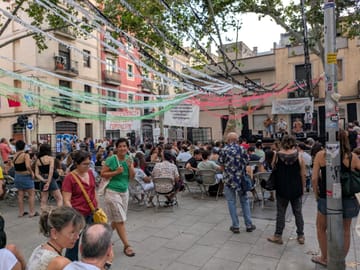 Crowd at a decorated street in Gràcia during the 2025 festival, with a bar set up on the pavement serving drinks under fairy lights.