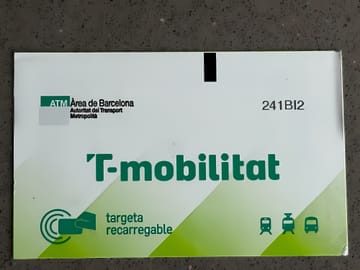 A contactless T-mobilitat card being tapped on a metro gate in Barcelona, with digital displays showing journey information.