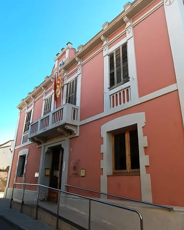 Exterior view of Sant Cugat del Vallès City Hall with flag flying, a modern administrative building surrounded by trees and walkways.