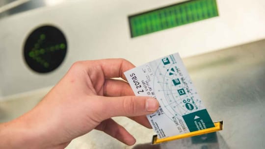 A T-Mobilitat card being tapped on a Barcelona Metro turnstile validator, with a metro train visible in the background.