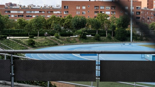 The Can Dragó athletics track in Barcelona, with its red running surface and green infield, surrounded by trees and buildings