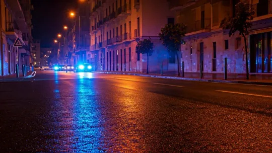 Emergency vehicle lights reflect on wet asphalt at night, symbolising a police operation.