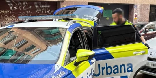 Police vehicle parked outside a building on a street in L'Hospitalet de Llobregat, with a closed metal shutter on the ground 