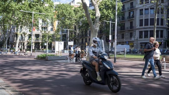 A motorcyclist drives through a pedestrianised section of Jardinets del Passeig de Gràcia in Barcelona, past people walking.