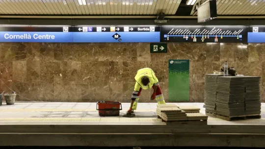Construction workers near a Barcelona metro station entrance with a sign indicating line closures.