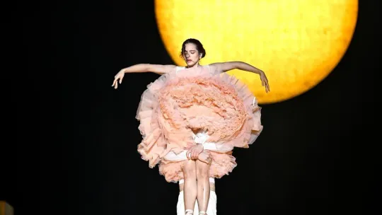 Rosalía performing on stage with bright lights, or a modern building in L'Hospitalet's Fira Gran Via area.