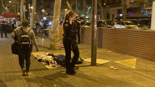 Street vendors quickly setting up makeshift stalls on a busy Barcelona street at night, with police officers in the backgroun