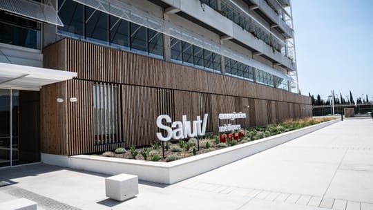 A modern, empty shuttle bus parked outside a large, contemporary building, possibly the new SEM headquarters in L'Hospitalet.