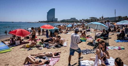 People relaxing on Bogatell beach in Barcelona, with parasols, towels, and the sea in the background.