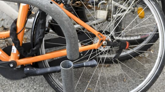 A bicycle secured to a U-inverted anchor on a Barcelona street, with other bikes and city buildings in the background.