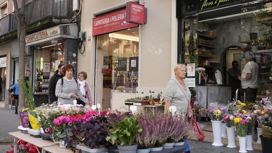 A person holding a shopping bag in front of a local shop in Barcelona, with a 'Bonus Consum' sign visible in the window.
