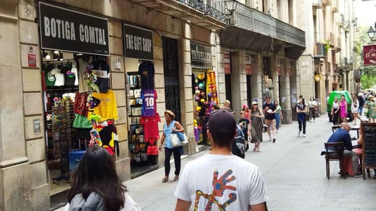 A busy street in Barcelona's Ciutat Vella district, showing historic buildings and a mix of commercial establishments.