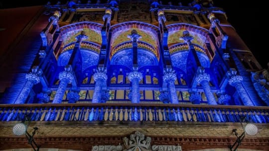 The Museu del Disseny de Barcelona (DHub) building illuminated in blue, with a large European Union flag unfurled in Plaça de