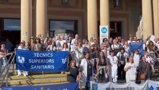 Healthcare technicians protest outside Hospital Vall d'Hebron in Barcelona, holding signs and banners.