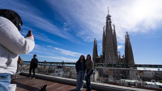 A panoramic view of Barcelona's Sagrada Família basilica with surrounding buildings and a clear sky, symbolising high tourist