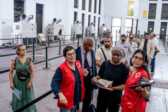People queuing outside a large building, possibly a convention centre, in Barcelona with signs in Catalan and Spanish.