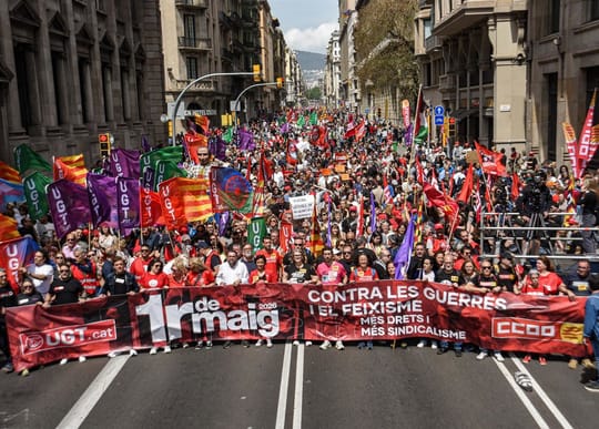 People marching in a May Day demonstration in Barcelona, holding union flags and banners on a city street.