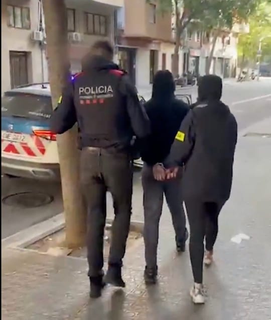 Police car with flashing lights on a Barcelona street at night, with Mossos d'Esquadra officers in uniform.