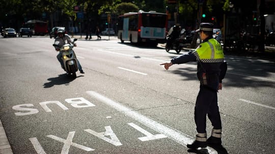Guàrdia Urbana officer on a motorcycle speaking to a moped rider in Barcelona city.