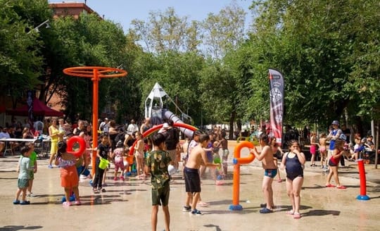 Children playing in a splash pad with water jets in a public park in Barcelona.