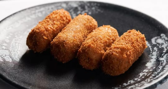 A close-up of a 'Barceloneta bomba' dish with aioli and bravas sauce, served on a white plate in a restaurant setting.