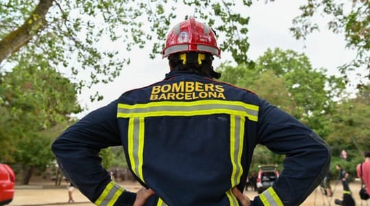 Firefighters in uniform standing next to a fire engine in a forest setting, with trees in the background.