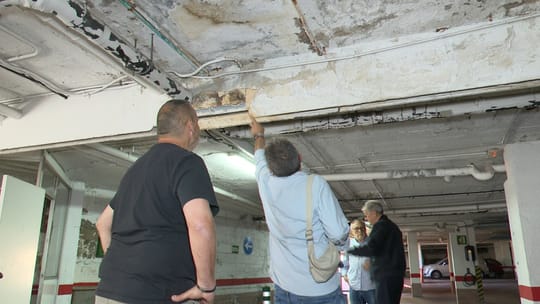 Water dripping from the ceiling onto a concrete floor in a dimly lit underground car park, with puddles forming.