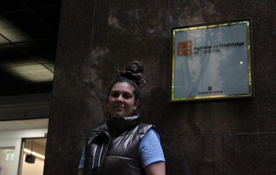 A woman with a child stands outside a residential building, looking concerned, representing families facing eviction.