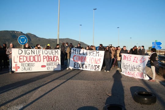 Teachers protesting in Barcelona, holding signs and banners, with police officers in the background.