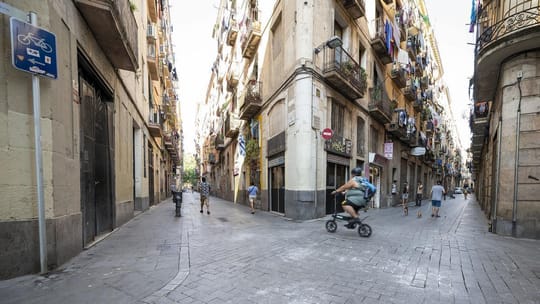A bustling street scene in Barcelona's Ciutat Vella district, showing historic buildings and pedestrians, symbolising urban r
