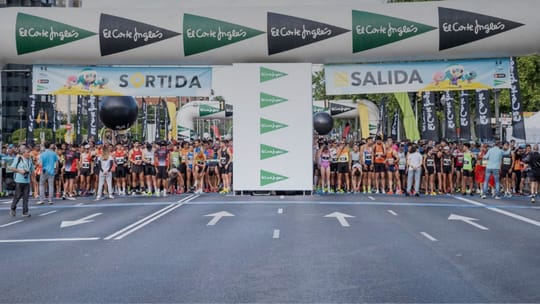 Runners participating in the Cursa El Corte Inglés race in Barcelona, with city buildings in the background.
