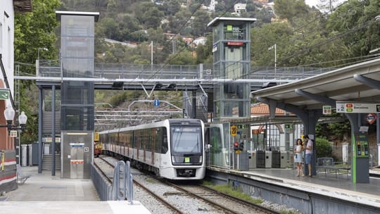 A modern FGC train platform with an escalator and a lift, showing accessibility features for commuters.