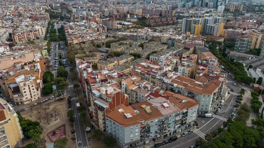 Aerial view of L'Hospitalet de Llobregat showing dense urban housing blocks and high-rise buildings under a clear sky.