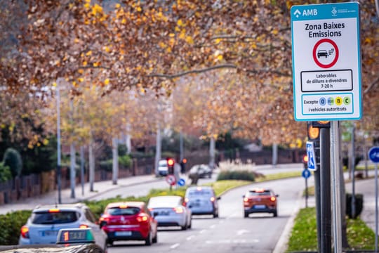 A street sign indicating a Low Emission Zone (ZBE) in Barcelona, with cars driving in the background.