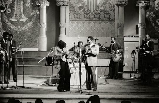 Miles Davis playing trumpet on stage, spotlight on him, audience in background.