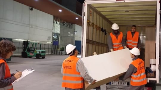 Volunteers sorting and moving donated furniture and materials from MWC26 in a warehouse.