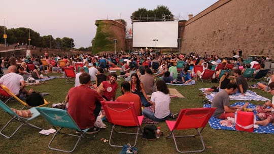 People watching an open-air film screening at Montjuïc Castle in Barcelona, with the city lights visible in the background.