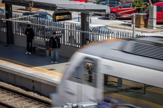 A Rodalies commuter train arriving at a station platform in Barcelona, with passengers waiting to board.