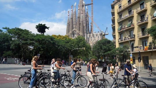 A view of Barcelona's iconic Sagrada Família basilica under construction, with cranes visible against a blue sky.