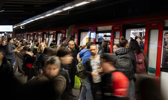 A Barcelona Metro train arriving at a station platform, with passengers waiting.