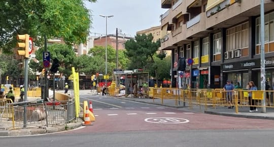 Construction barriers and machinery on a city street with buildings in the background.