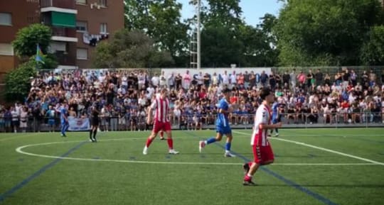 Two football teams, one in blue and one in red, competing for the ball on a green pitch during a match in Barcelona.