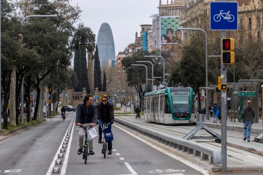 A modern Barcelona tram travels along a street with buildings and trees in the background.