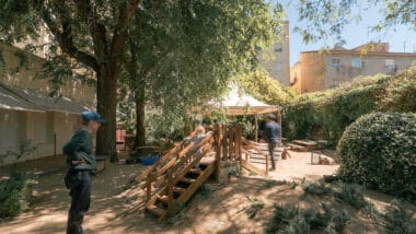 A shaded playground area with children playing, representing a climate shelter in Barcelona's Nou Barris district.