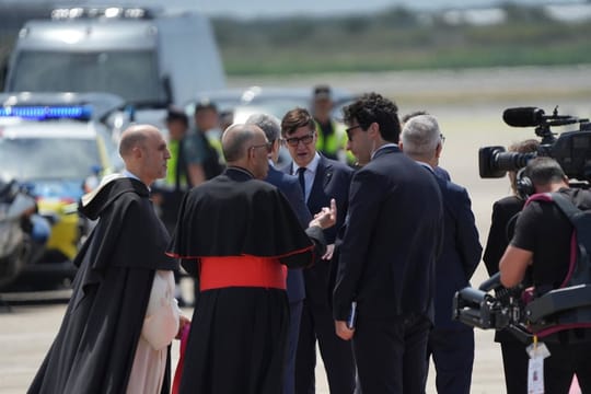 Pope Leo XIV walking on a red carpet after disembarking an Iberia plane at Barcelona-El Prat Airport, greeted by a line of of